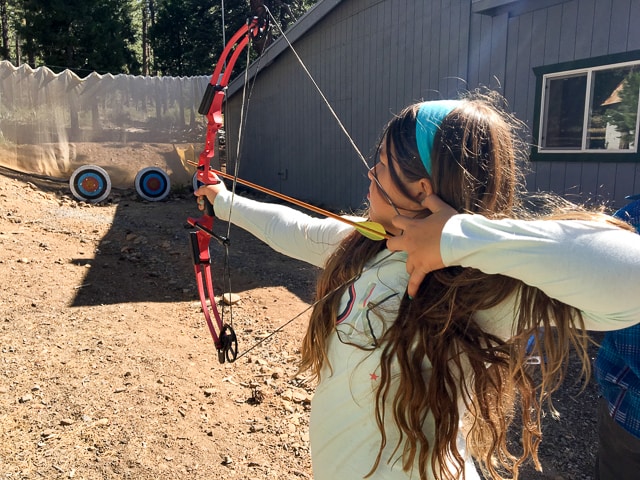 girl drawing back a bow and aiming for a target