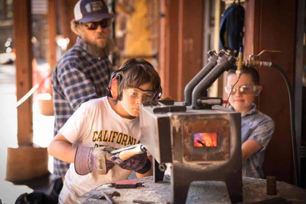teacher watching student work a forge