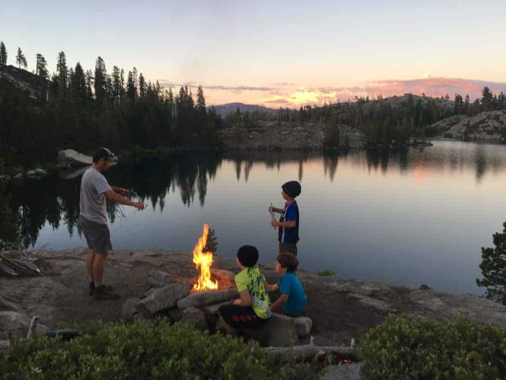 boys backpacking crew around a lakeside campfire