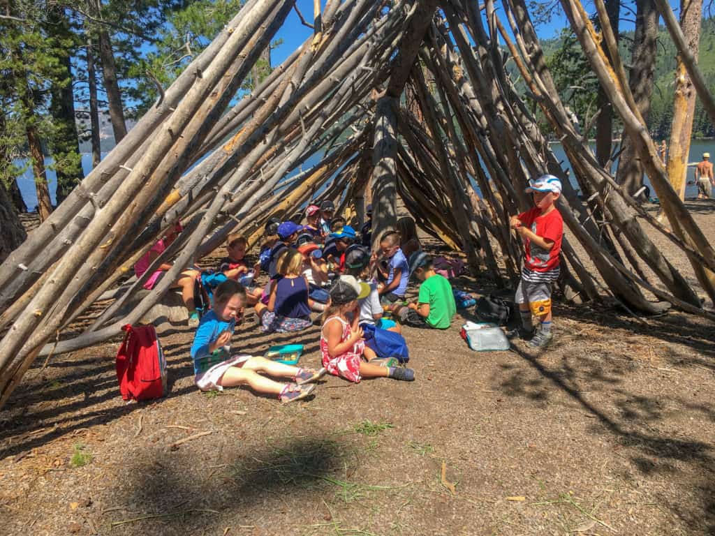 elementary students inside a tent made of logs