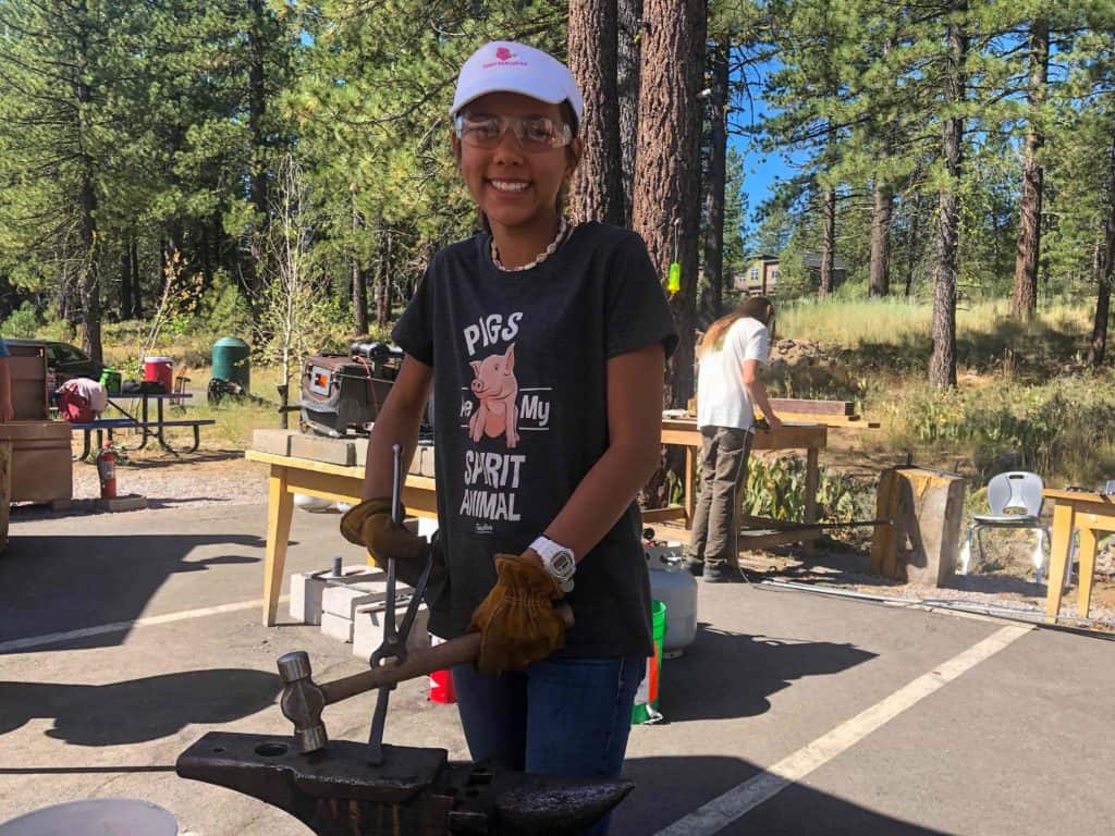 student smiling in fornt of an anvil
