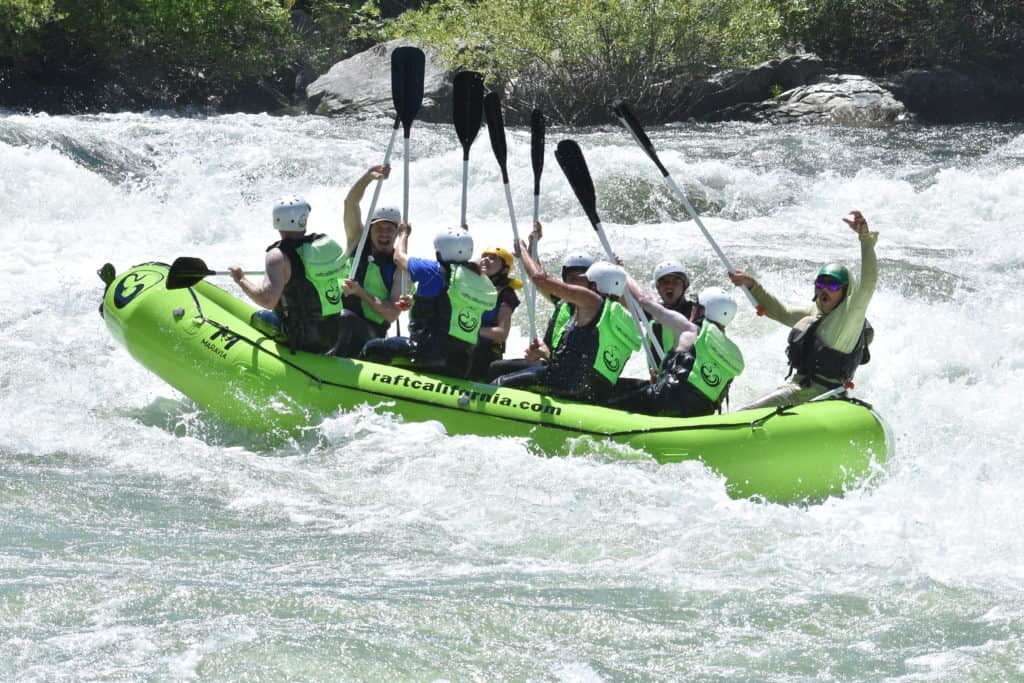 students and teacher in a raft holding up their oars